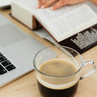 Woman Sitting at the Desk with a Laptop and a Cup of Coffee while Using a Paper Dictionary